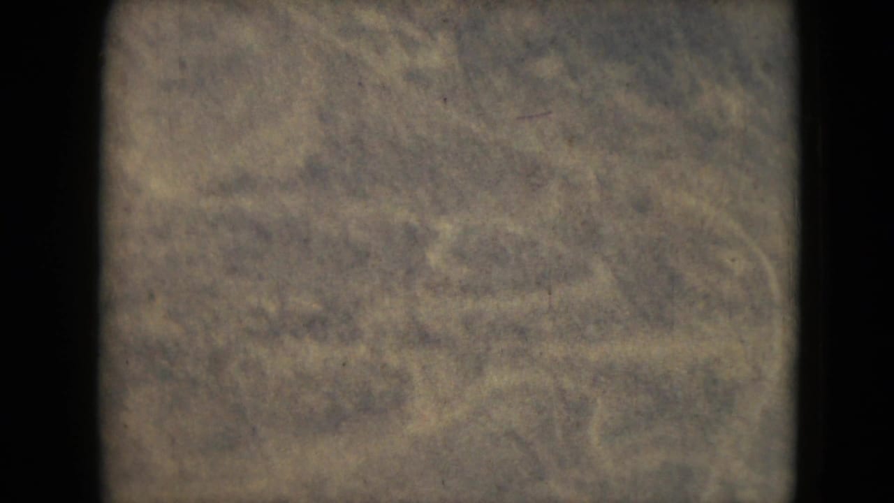 Soft aerial view of scrub-covered ground with faint trails and heavy film grain.