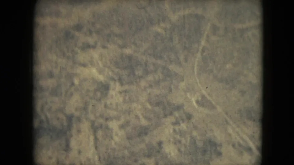 1962 8mm aerial view near Mexico City with patchy dry vegetation, pale ground lines, grain, and a dark vertical film border.
