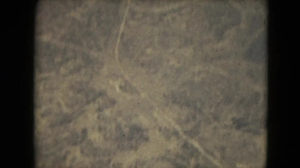 1962 8mm aerial frame from the Mexico City area showing dry scrub terrain, faint winding paths, scratches, and aged color fading.