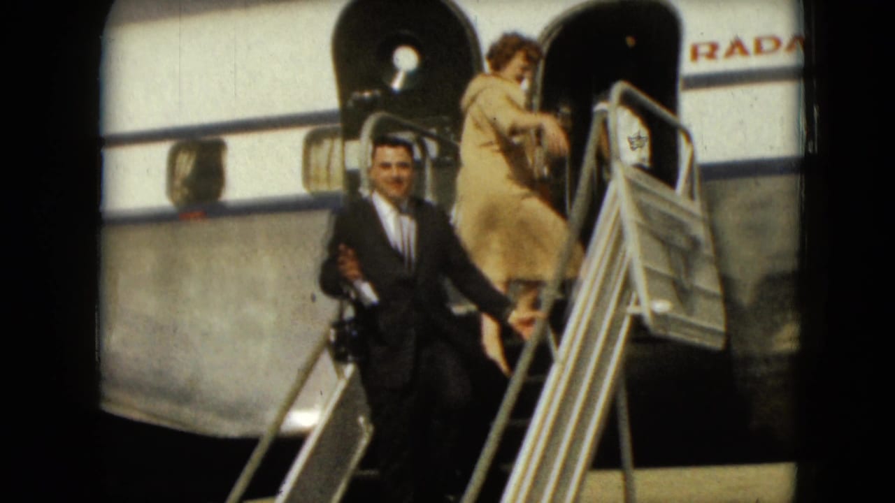 Man in a dark suit stands on airplane stairs as a woman boards above him.