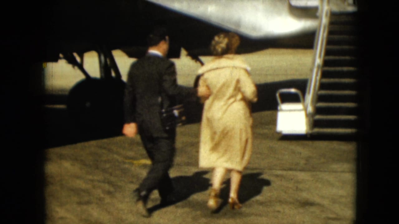Man and woman walk across the tarmac toward aircraft stairs beside a plane.