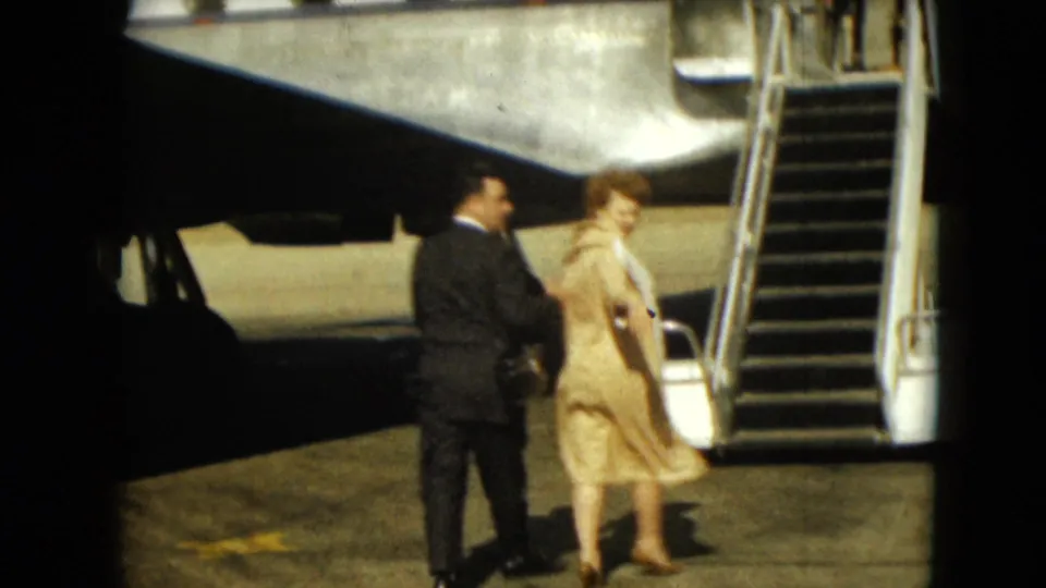 The couple reaches the boarding area beside the aircraft stairs, with the woman partly turned toward the camera.
