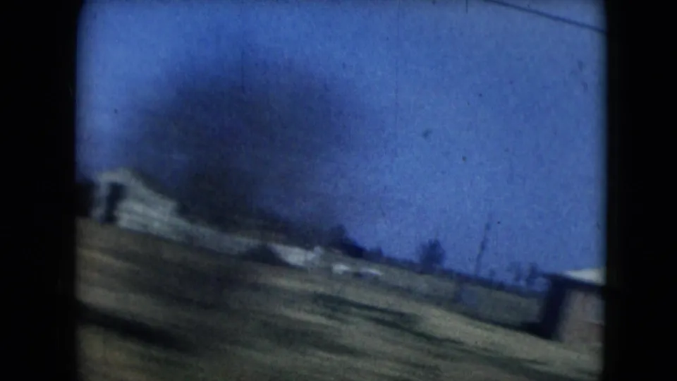 1962 Mexico City home-movie frame showing a blurred roadside house, open yard, and blue sky from a moving car.