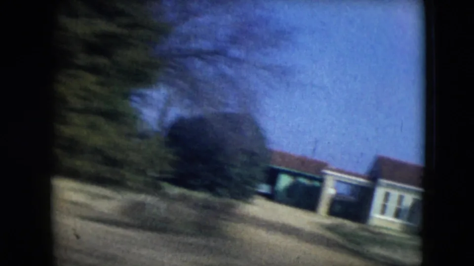1962 Mexico City residential street view with low houses, trees, and a tilted moving-car perspective.