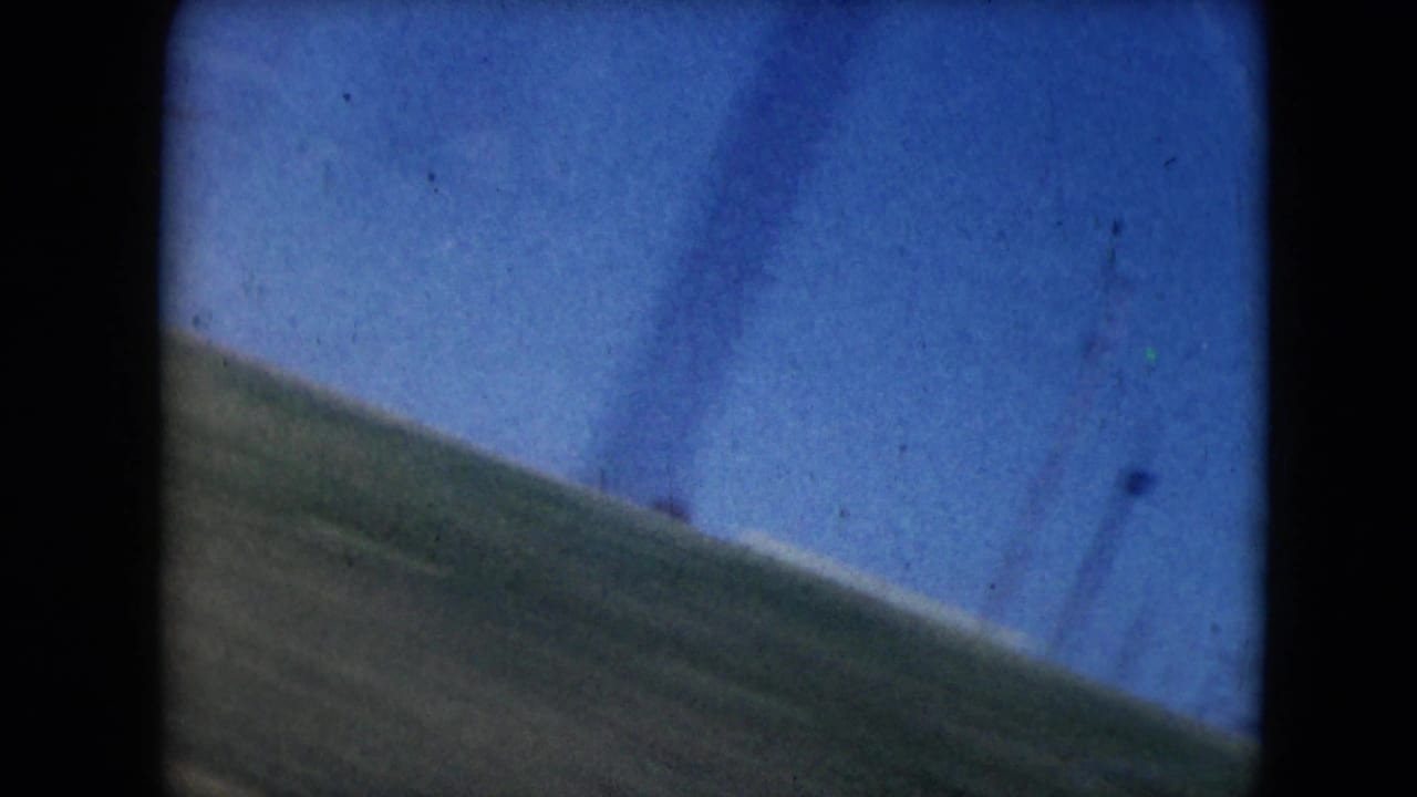 Blurred grassy hillside and blue sky framed by dark film edges during a fast roadside pass.
