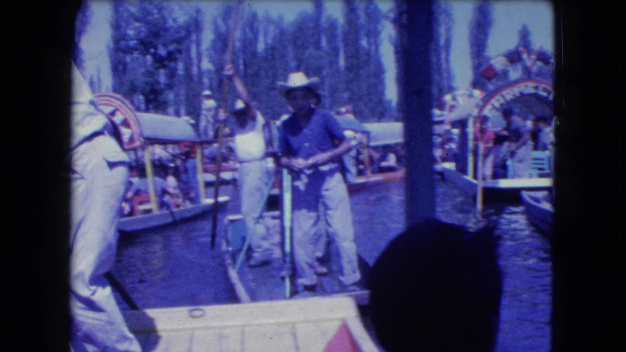 1962 Mexico City home-movie frame showing men in cowboy hats and light clothing working poles near trajineras on a canal.