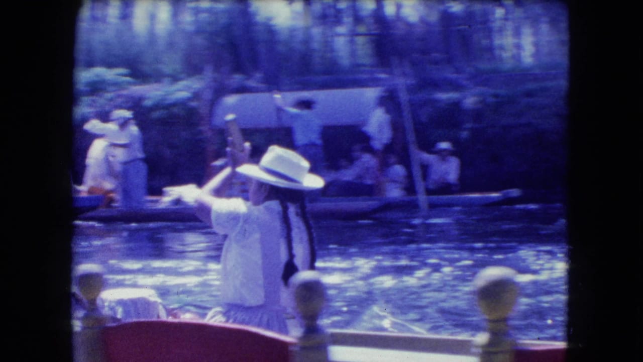 1962 Mexico City canal scene with a white-hatted rower in a narrow boat near other passengers and moored excursion boats.