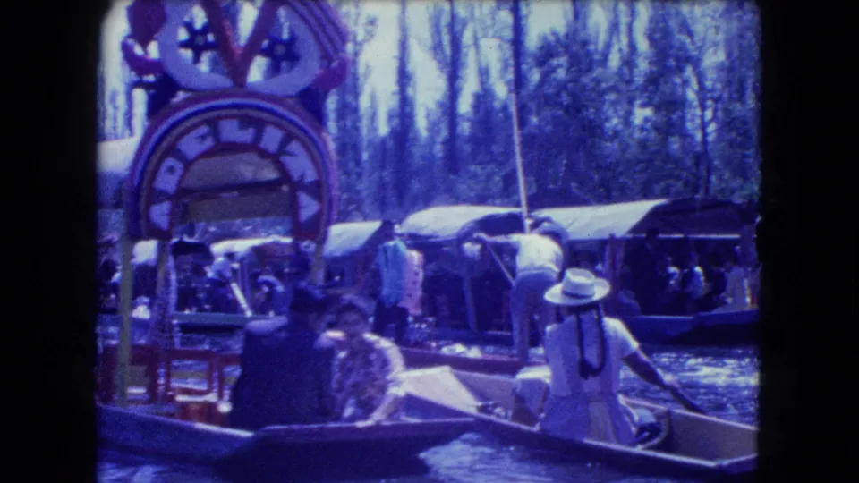 1962 Mexico City canal footage shows a painted arch sign, tourists, a rower, and multiple excursion boats on the water.