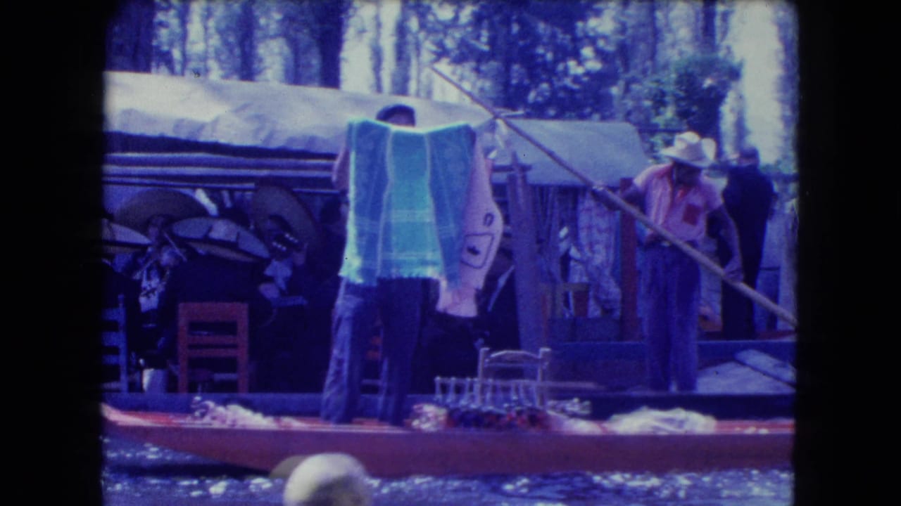 Adults stand in a wooden boat near towels, chairs, and canal water.
