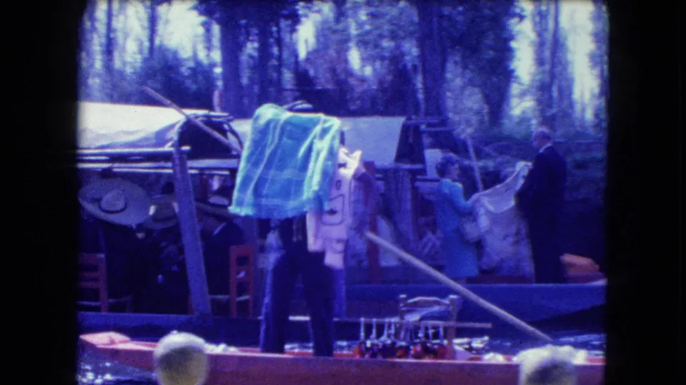 1962 Mexico City 8mm view of a canal boat with draped textiles, seated and standing adults, chairs, and water in the foreground.