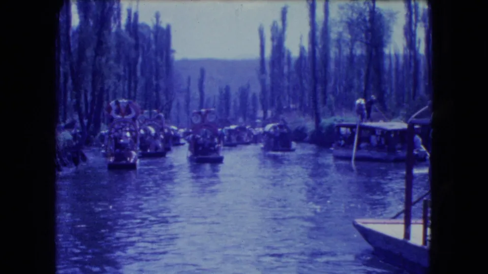 Decorated trajineras and small boats appear on a Mexico City canal in blue-shifted 8mm footage.