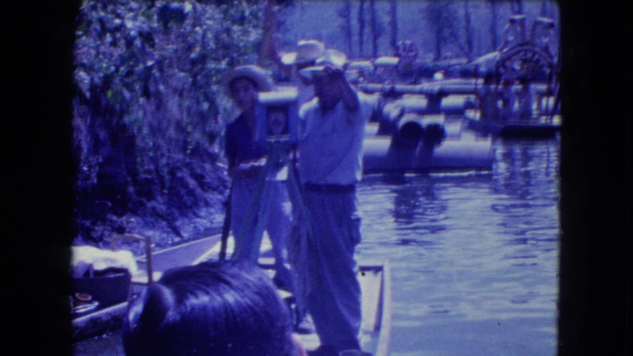 1962 Mexico City canal footage showing a man in a straw hat using a large tripod camera from a boat near other trajineras.