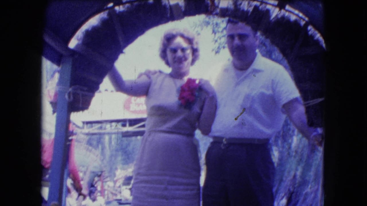 Couple posing beneath an arched structure beside water.