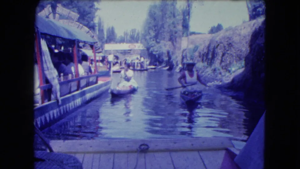 A visitor-shot 1962 Mexico City canal view shows two small paddled boats near a larger covered passenger craft.