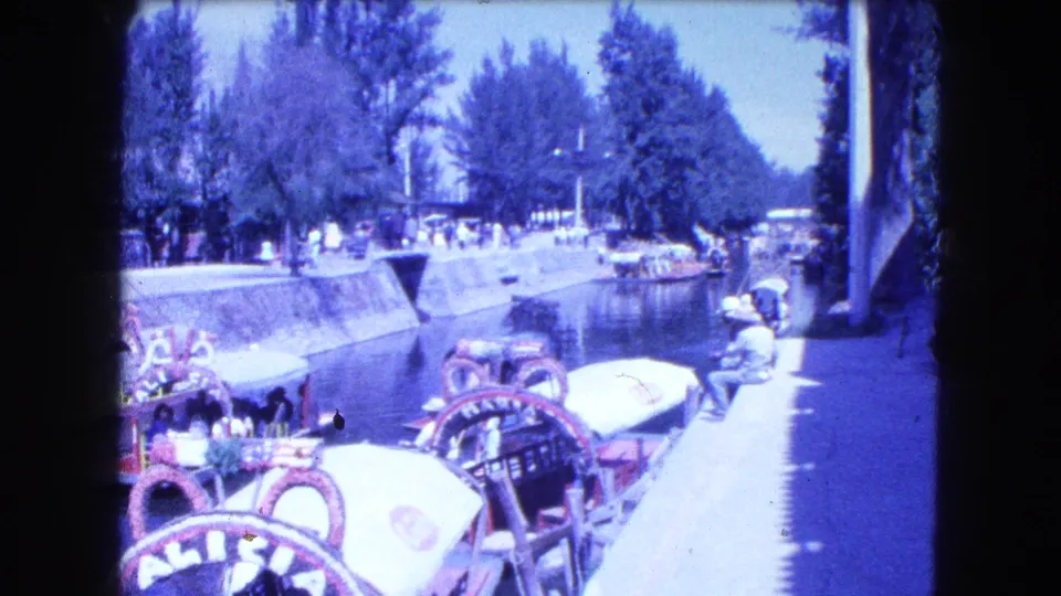 Mexico City canal footage from 1962 with ornate boats, visible passengers, pedestrians, trees, and strong blue-purple 8mm color shift.