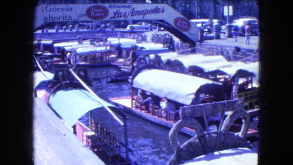 Trajineras and visitors appear on a canal beneath visible Las Amapolas restaurant signage in Mexico City footage.