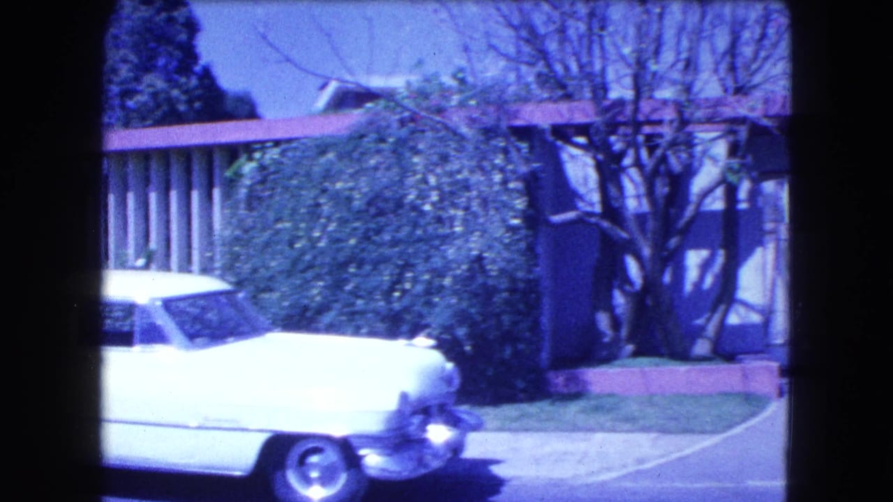 1962 Mexico City street view of a white rounded sedan with chrome trim parked in front of hedges and a mid-century fence.
