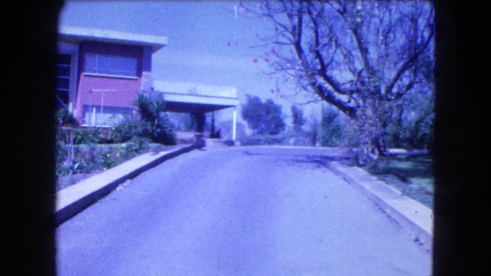 1962 Mexico City frame with a residential driveway, mid-century house facade, carport area and tree-lined garden edge.