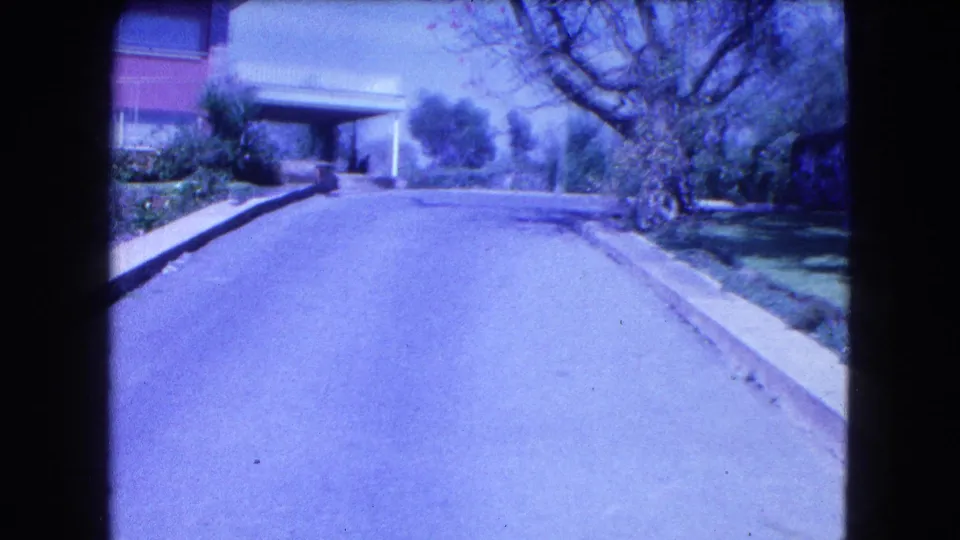 1962 Mexico City frame capturing the residential approach with broad driveway, carport, garden planting and trees in blue-tinted 8mm color.