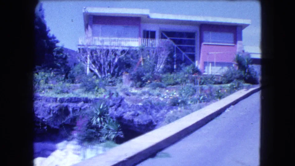1962 Mexico City home-movie view of the residence, balcony, pink facade, dense plantings, and driveway leading uphill.