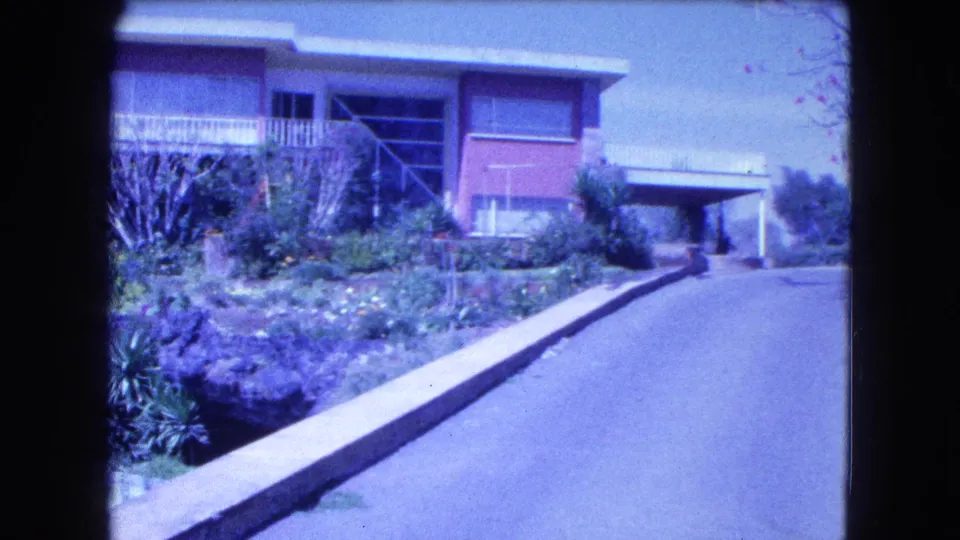 1962 Mexico City frame showing the hillside house, planted garden, driveway, and carport at the right edge.