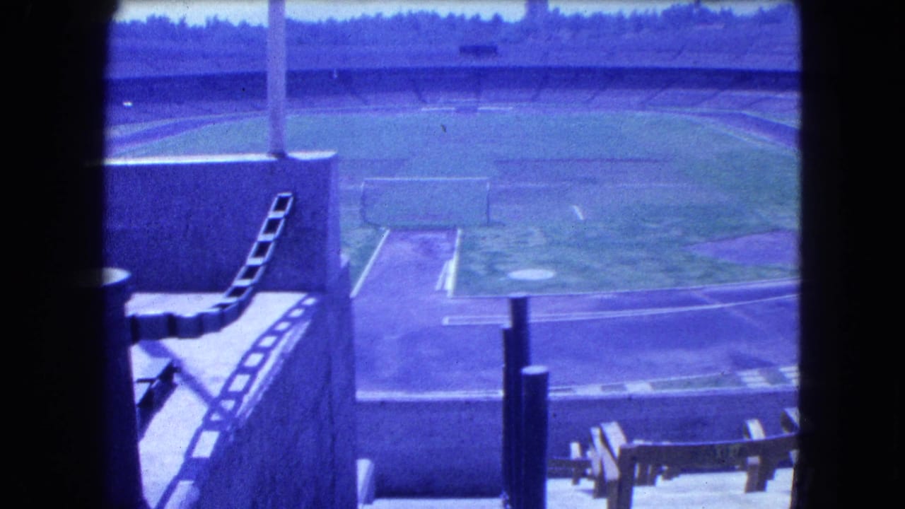 1962 Mexico City home-movie frame showing a bright playing field from above, with concrete barriers, a ladder, and distant trees.