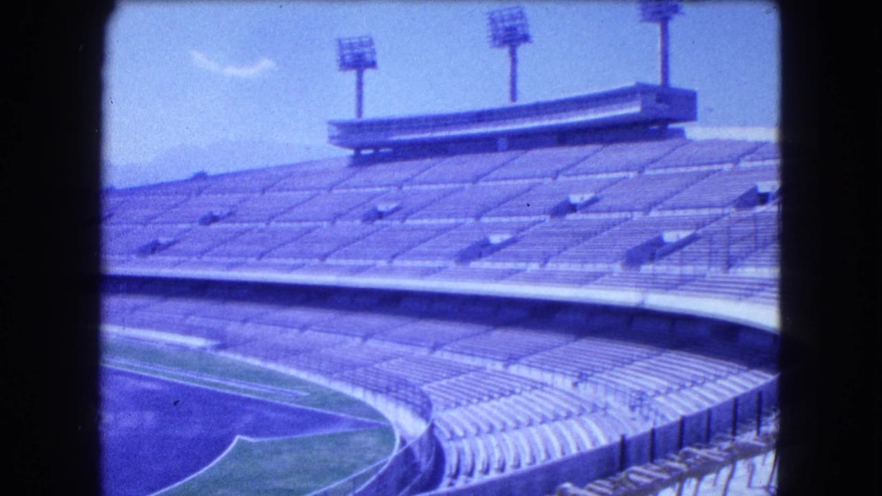 Empty stadium seating curves around a running track and field under a hazy sky.