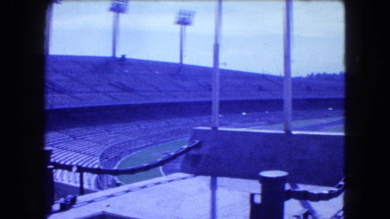 Curving stadium stands, field edge, and several tall floodlight poles.