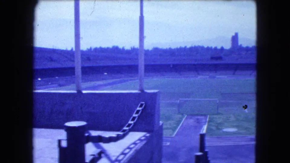 Blue-tinted final frame of the Mexico City stadium showing empty field areas, floodlight poles, railings, and distant hills or skyline.
