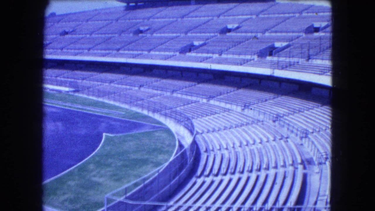 1962 8mm view of a large Mexico City stadium with curved concrete stands, a strip of green field, and dark frame edges.