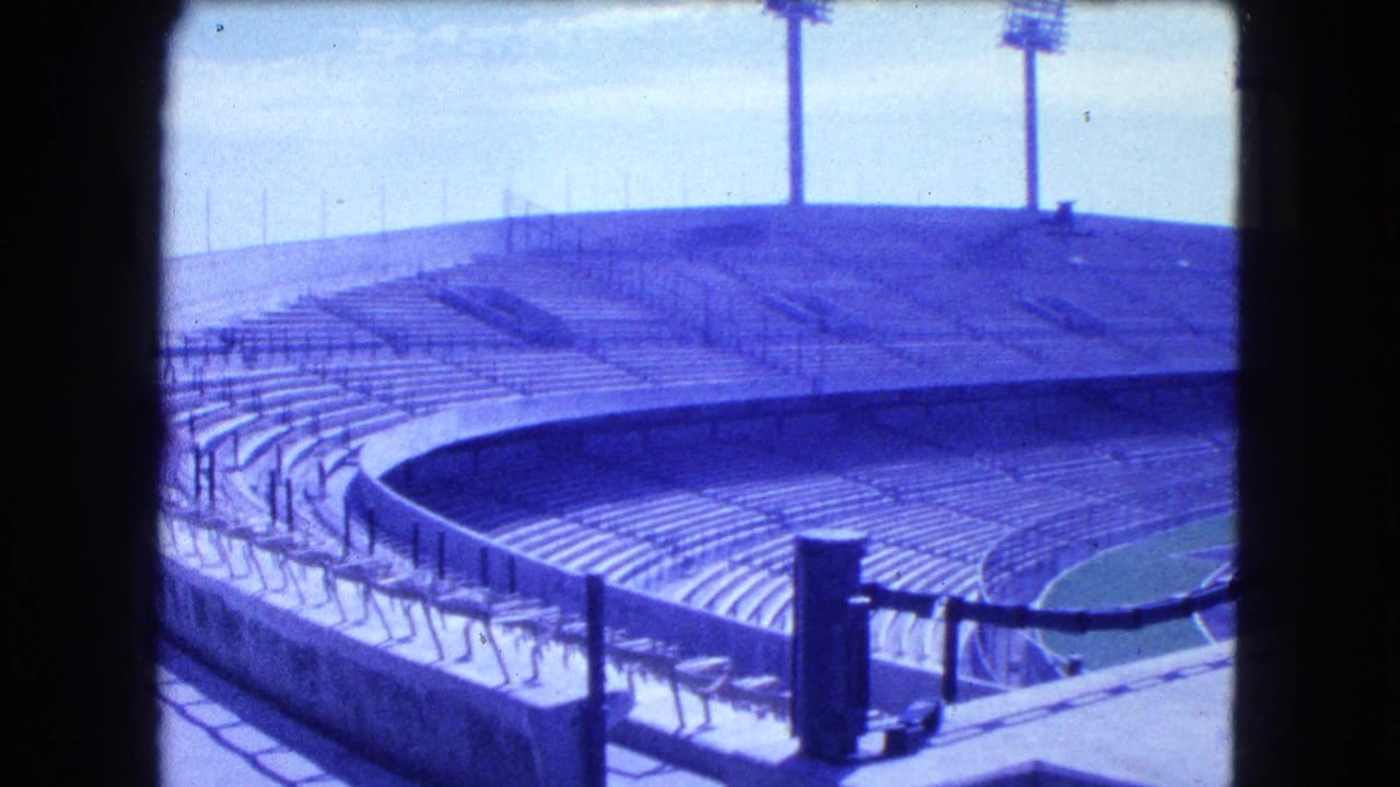 Empty stadium stands with railings, floodlight towers, and dark frame edges.