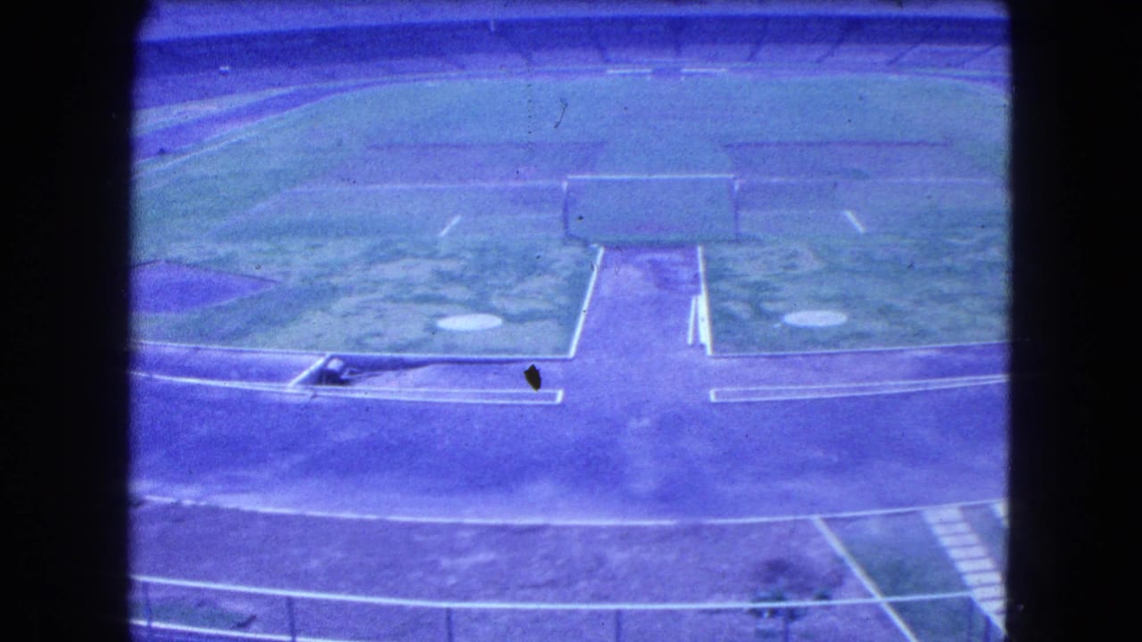 Elevated view of a grassy sports field, running track, and empty stadium seating.