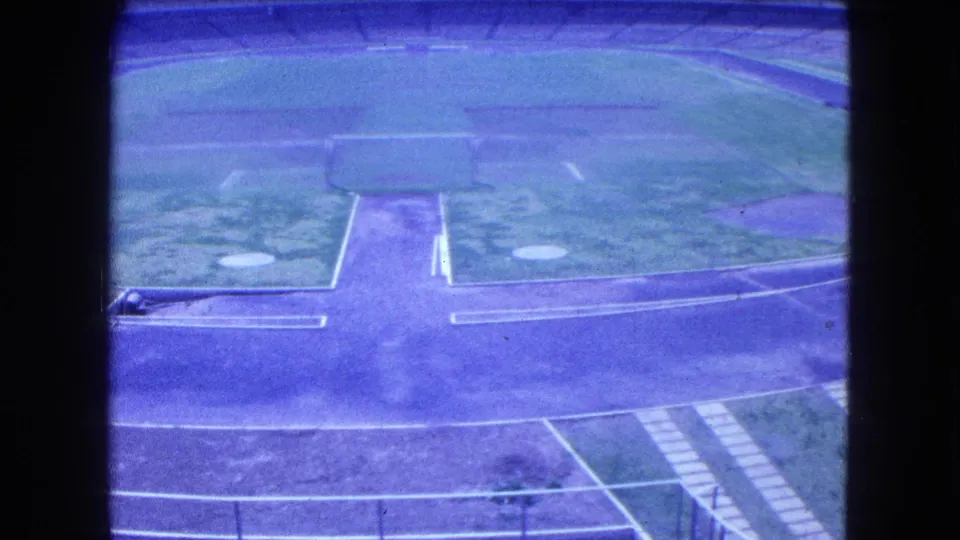 Home-movie frame of the Mexico City sports arena, showing the grass field, track curve, and empty seating from above.