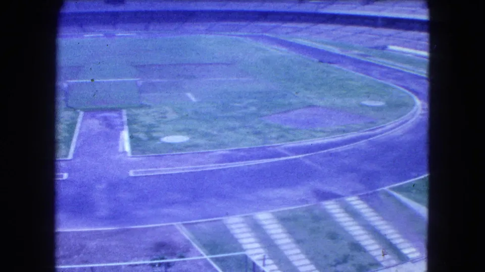 1962 Mexico City arena view with a grassy field, track, walkway, and empty stadium seating under bright daylight.