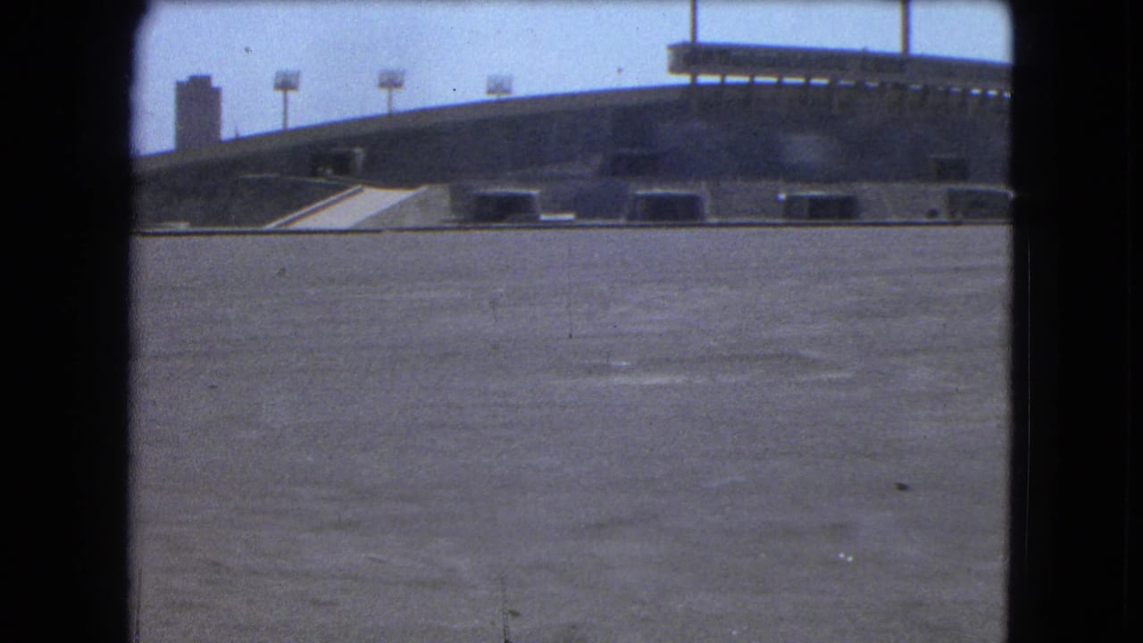 Wide paved foreground with an elevated concrete ramp or bridge and distant buildings under a pale sky.