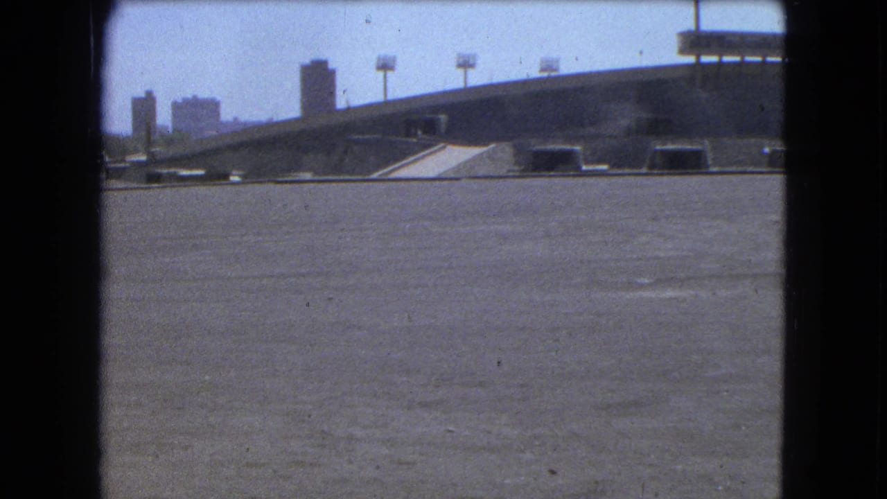 1962 Mexico City 8mm view of an elevated concrete structure, open pavement, rooftop lights, and distant mid-century buildings.
