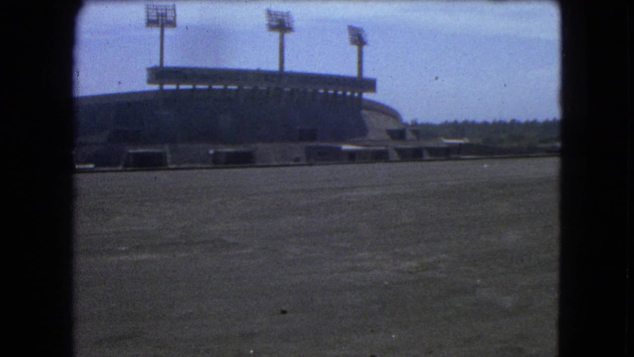 1962 Mexico City 8mm frame showing an empty stadium view with concrete foreground, curved stands, and tall floodlights.