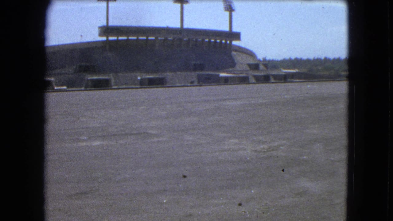 Wide view of an empty stadium with floodlight poles above a concrete field.