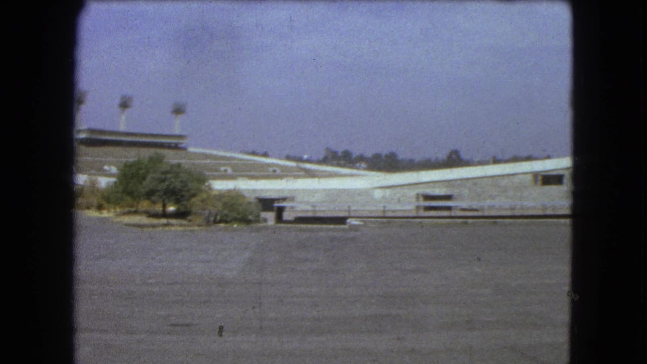 Wide view of an empty stadium structure with light towers and small trees in front.