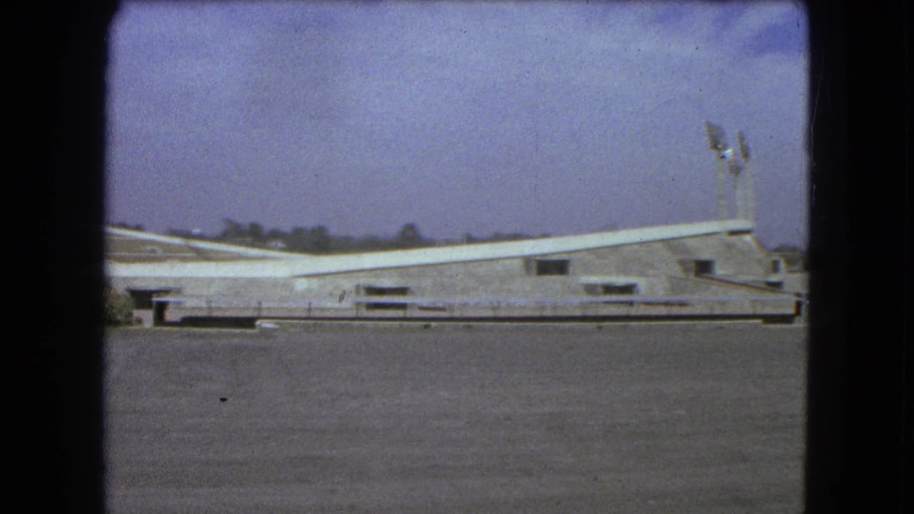 Wide 1962 Mexico City view of the stadium exterior, showing its sweeping roofline, light towers and open paved area.