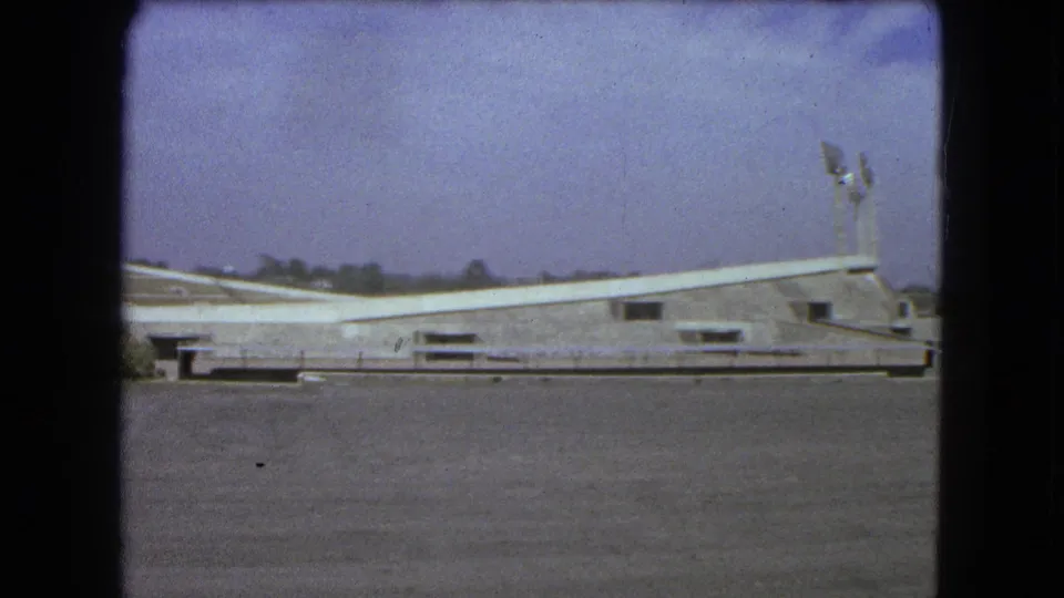 Wide 1962 Mexico City view of the stadium exterior, showing its sweeping roofline, light towers and open paved area.