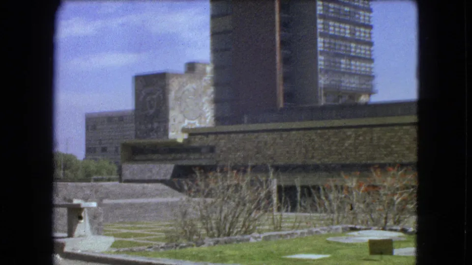 1962 Mexico City exterior with steps, patterned paving, a modern stone venue, mural panels, shrubs, and high-rise buildings.