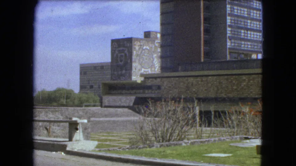 Mexico City park scene from 1962 with lawn, shrubs, steps, modernist venue walls, mural panels, and urban towers in the background.