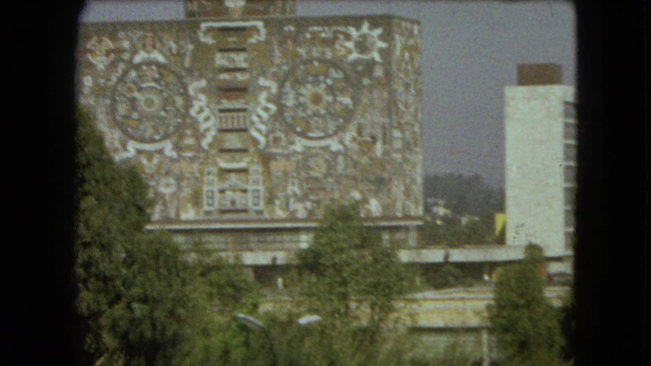 1962 Mexico City view of a large building facade with intricate mural patterns, partly obscured by trees and a dark foreground frame.