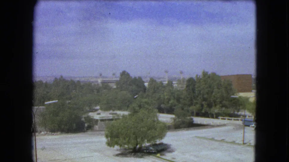 1962 Mexico City 8mm frame showing treetops, broad paved areas, low modern buildings, and a hazy distant skyline.