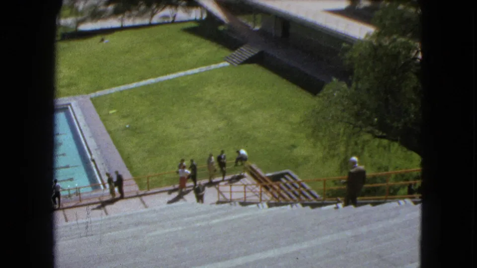 1962 Mexico City 8mm view of people on broad stairs near a pool, with lawns and a low modernist campus building beyond.
