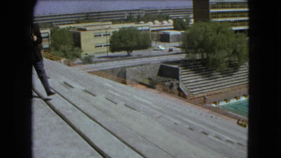 1962 Mexico City 8mm frame looking over concrete terraces, roadways, trees, bleachers, and modern urban buildings.