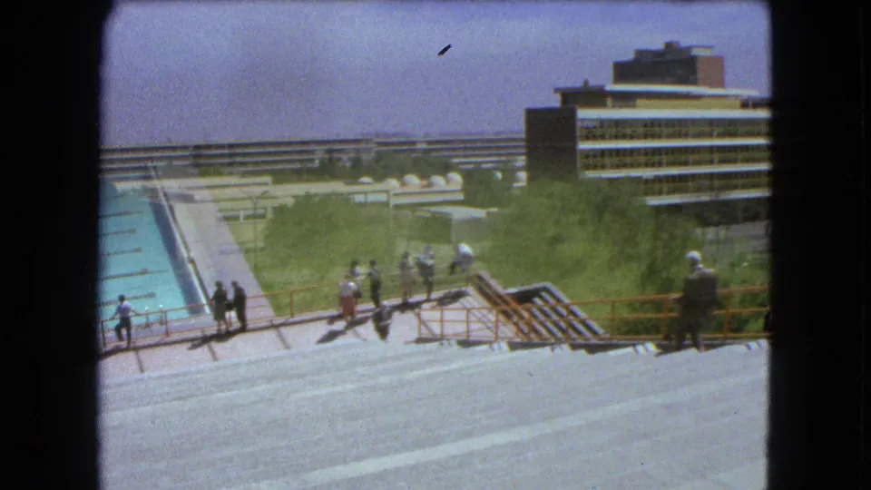1962 Mexico City view of a swimming pool and concrete terraces with small groups of people near trees and modern buildings.