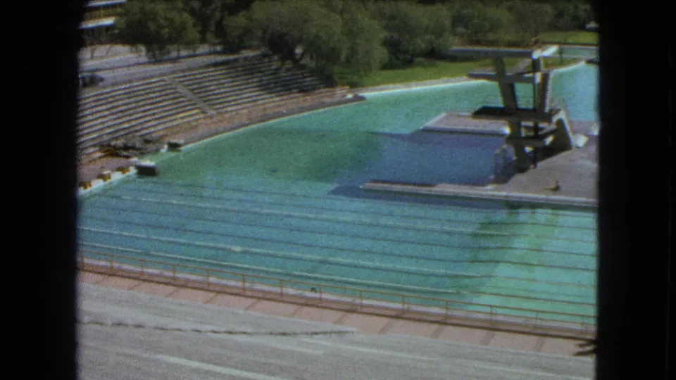1962 Mexico City pool complex seen from above, with empty bleachers, swimming lanes, diving platforms, trees, and deck area.