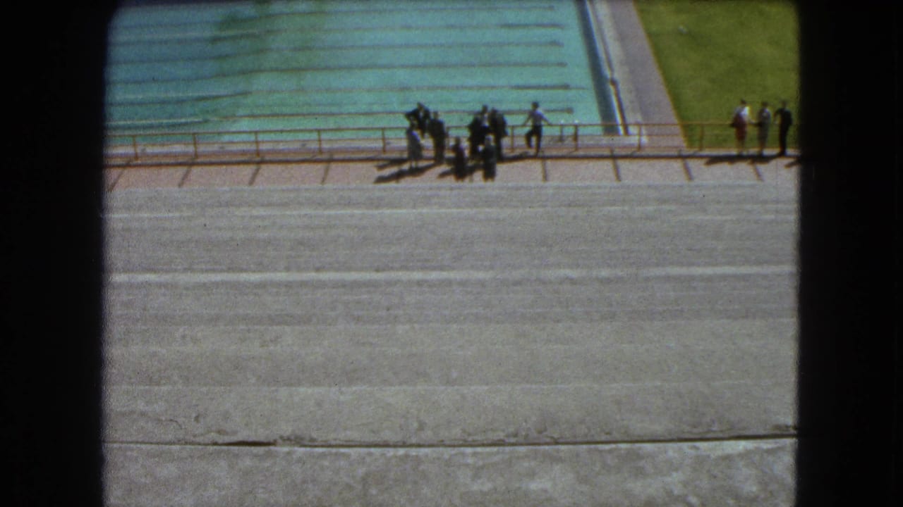 1962 Mexico City 8mm frame showing a large outdoor pool, paved deck, railing, and a small group of people seen from above.